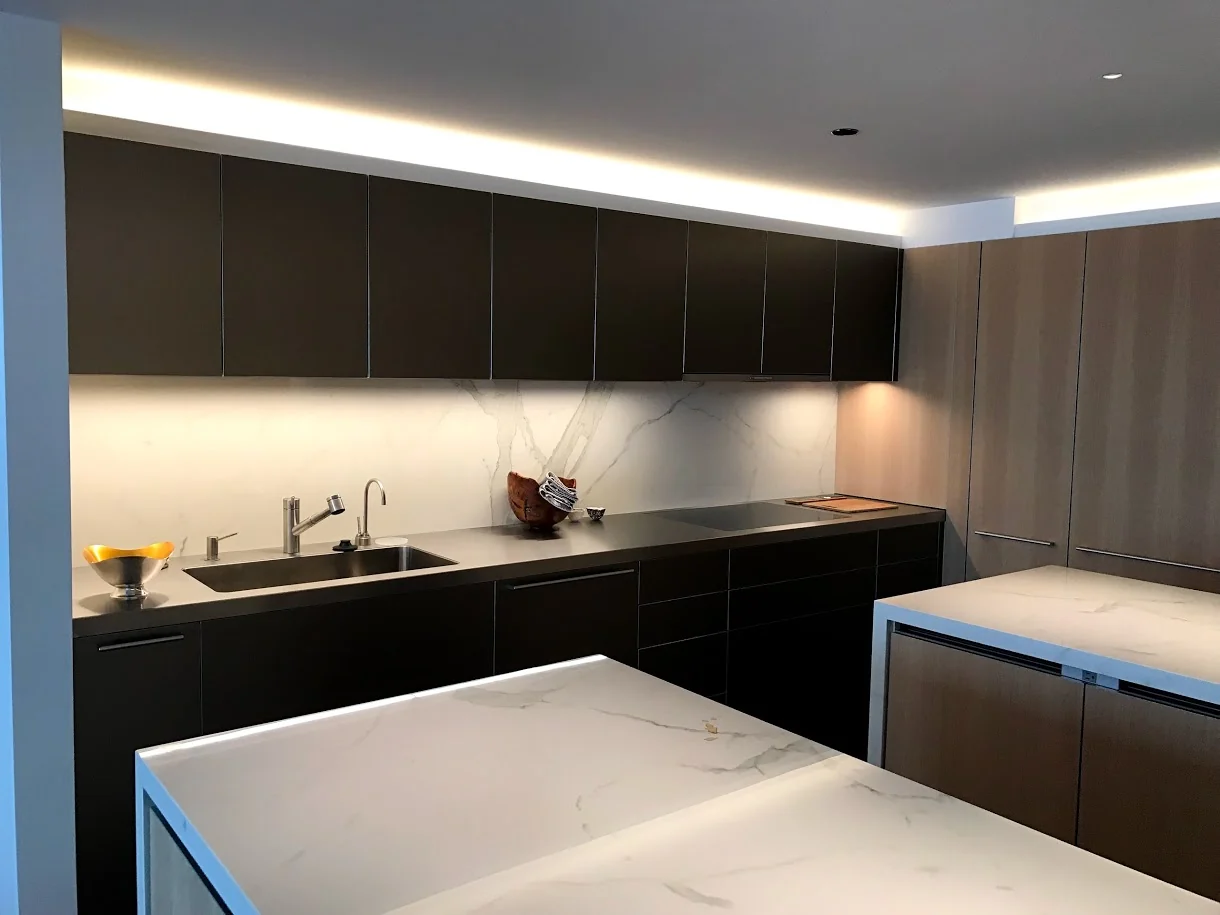 Pale veined countertop and illuminated backsplash beside dark cabinets